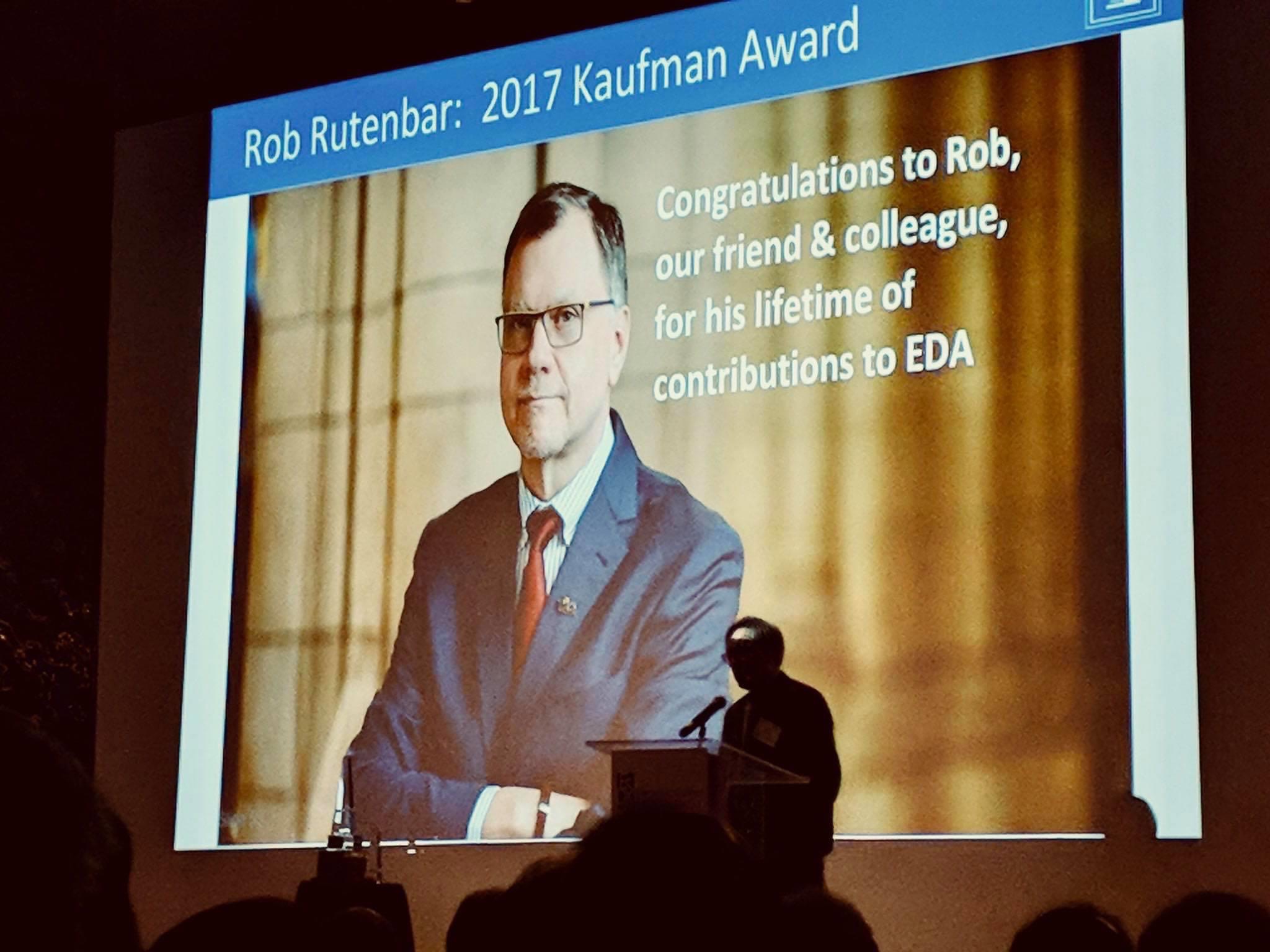 Photo of the Kaufman EDA Award ceremony, 2018. The photo shows a projector screen with an image of Rutenbar and the words, "Congratulations to Rob, our friend and colleague, for his lifetime of contributions to EDA". 